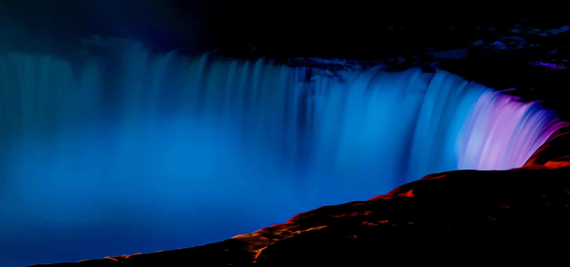 De beroemde Niagara wattervallen worden in de avond spectaculair verlicht in mooi wit, blauw en roze licht.